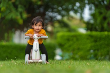 Mutlu küçük kız parkta plastik bir motosiklet oyuncağı sürüyor.