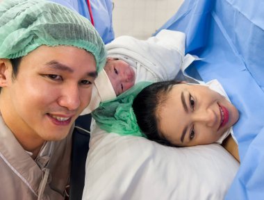 first sight of father and mother with their newborn baby after the Cesarean section in operation room. happy family concept clipart