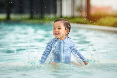 Mutlu bebek yüzme havuzunda su sıçratarak oynuyor.