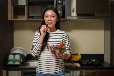 Kadın ev mutfağında sağlıklı meyve yiyor. 