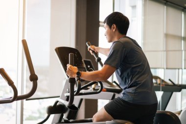 Spor jimnastik salonunda eliptik bir çapraz antrenör üzerinde egzersiz yapan genç adam. 