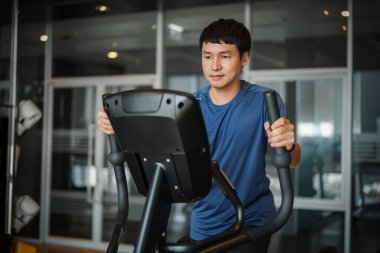 Spor jimnastik salonunda eliptik bir çapraz antrenör üzerinde egzersiz yapan genç adam. 