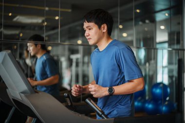 Spor salonunda koşu bandında koşan genç adam.