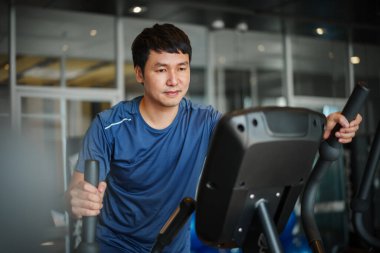 Spor jimnastik salonunda eliptik bir çapraz antrenör üzerinde egzersiz yapan genç adam. 