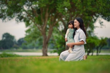 Mutlu anne, küçük kızıyla parkta çimlerin üzerinde oturuyor.