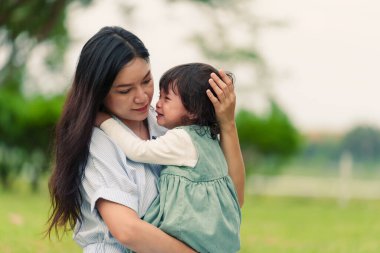 Anne, ağlayan bebeğini parkta çimen tarlasında kucağına alıp rahatlatıyor.