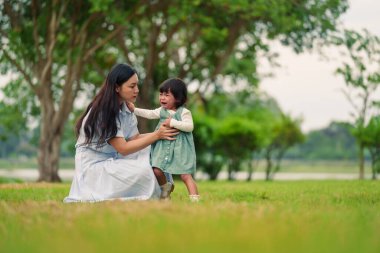 Anne, ağlayan bebeğini parkta çimen tarlasında kucağına alıp rahatlatıyor.