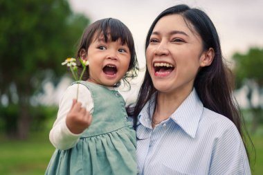 Mutlu anne kucağında ve gülüyor parkta çimen tarlasında yeni yürümeye başlayan bebekle