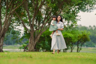 Mutlu anne, parkta çim tarlasında yürürken bebeğini kucağında tutuyor.
