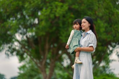 Mutlu anne, parkta çimlerin üzerinde küçük bir kızı kucağında tutuyor.