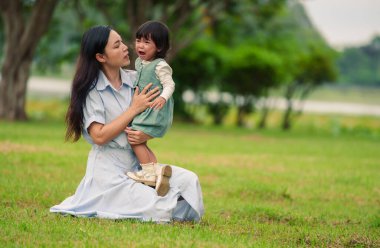 Anne, ağlayan bebeğini parkta çimen tarlasında kucağına alıp rahatlatıyor.