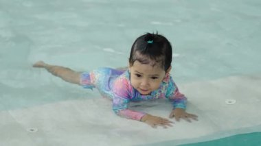 Küçük kız havuzun kenarında yüzmeyi öğreniyor.