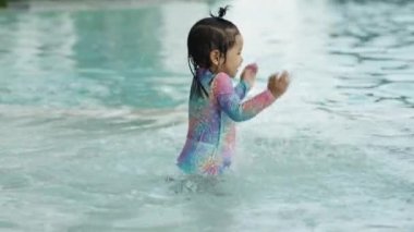 Mutlu küçük kız yüzme havuzunda su sıçratma oyunu oynuyor.