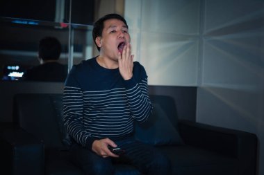 Uykulu adam geceleri kanepede televizyon izlerken esniyor.