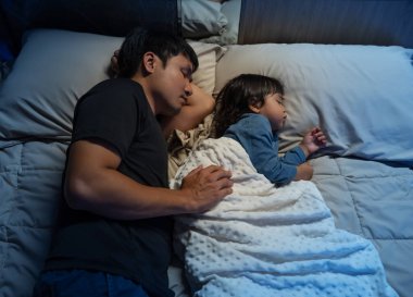 Baba, yeni yürümeye başlayan bebeği kucaklar. Geceleri yatakta birlikte uyur.