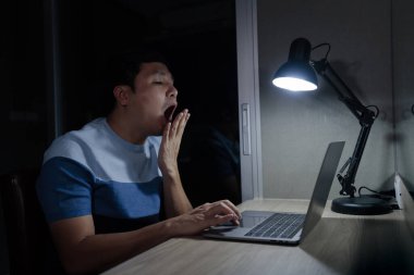 Uykulu adam geceleri dizüstü bilgisayarla çalışırken esniyor.