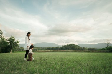 Mutlu anne yeni yürümeye başlayan kızıyla çim tarlasında yürüyor