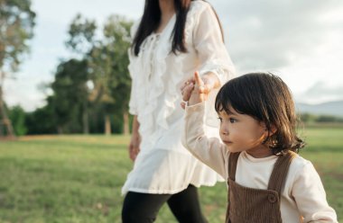 Küçük bebek annesinin elini tutuyor ve çim tarlasında yürüyor.