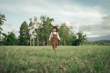 Mutlu küçük kız çimlerde yürüyor.