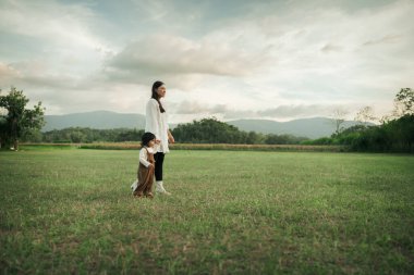 Mutlu anne yeni yürümeye başlayan kızıyla çim tarlasında yürüyor