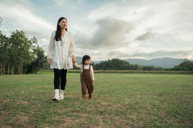 Mutlu anne yeni yürümeye başlayan kızıyla çim tarlasında yürüyor