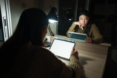 Bir gece beyaz ekranlı dijital tabletle çalışırken düşünen kadın