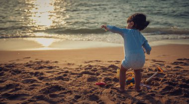 Küçük kız Pattaya, Tayland 'da gün batımında kumsalda kum oyuncağı oynuyor.