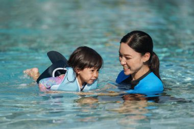 Anne, bebeğe havuzda yüzmeyi ve can yeleği giymeyi öğretiyor.
