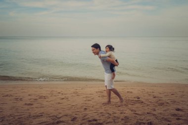 Baba, Pattaya, Tayland 'da deniz kıyısında yürüyen küçük bebeğe sırtına biniyor.