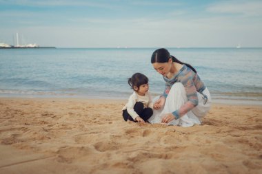 Küçük mutlu kız Pattaya, Tayland 'da annesiyle kumsalda kum oynuyor.