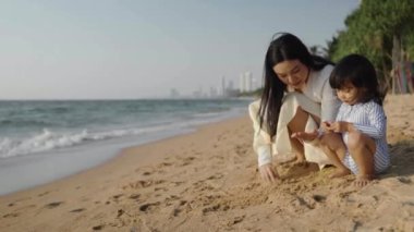 Anne ve küçük bebek Tayland 'ın Pattaya sahilinde deniz kabuğuyla oynuyorlar.