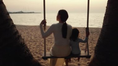 Anne ve küçük bebek, Tayland 'ın Pattaya şehrinde gün batımında, deniz kıyısında salıncakta sallanıyor.