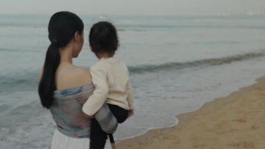 Pattaya, Tayland 'da deniz sahilinde annesinin küçük bebekle sarılıp konuşması ağır çekimde.