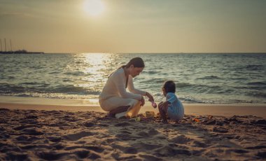 Pattaya, Tayland 'da gün batımında annesiyle kumsalda kum oyuncağı oynayan mutlu bir bebek.