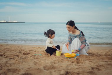 Küçük mutlu kız Pattaya, Tayland 'da annesiyle kumsalda kum oyuncağı oynuyor.