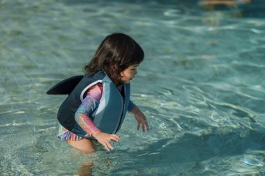 Bebek ceketli mutlu bebek yüzme havuzunda su oynuyor.