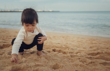 Küçük kız Pattaya, Tayland 'da kumsalda kum oynuyor.