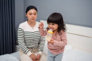 Yeni yürümeye başlayan kız annesiyle birlikte şişeden süt içiyor.