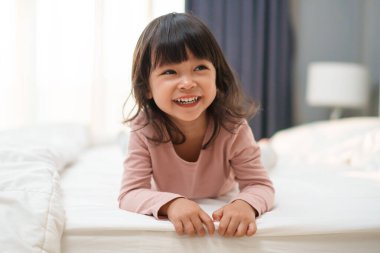 Neşeli küçük kız yatakta oynuyor ve gülüyor.