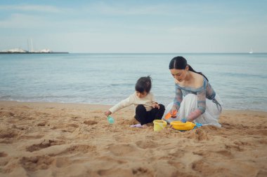 Küçük mutlu kız Pattaya, Tayland 'da annesiyle kumsalda kum oyuncağı oynuyor.
