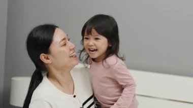 Neşeli anne ve küçük kız bir yatakta oynuyorlar.