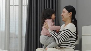 Neşeli anne ve küçük kız bir yatakta oynuyorlar.