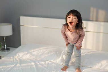 Neşeli küçük kız yatakta oynuyor ve gülüyor.