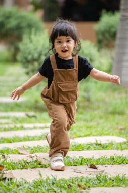 Mutlu küçük kız bahçede taş bir yolda yürüyor.