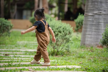 Küçük kız bahçede taş bir patikada yürüyor.