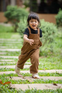 Mutlu küçük kız bahçede taş bir yolda koşuyor.