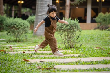 Mutlu küçük kız bahçede taş bir yolda yürüyor.