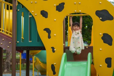 Parktaki çocuk parkında sarı barı elinden tutan mutlu küçük kız.