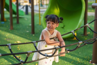 Parktaki çocuk parkında tırmanma halatlarıyla oynayan mutlu bir kız.