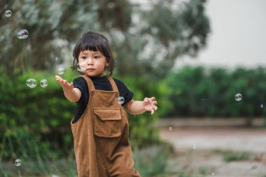 Küçük kız parkta sabun köpüğü oynuyor.